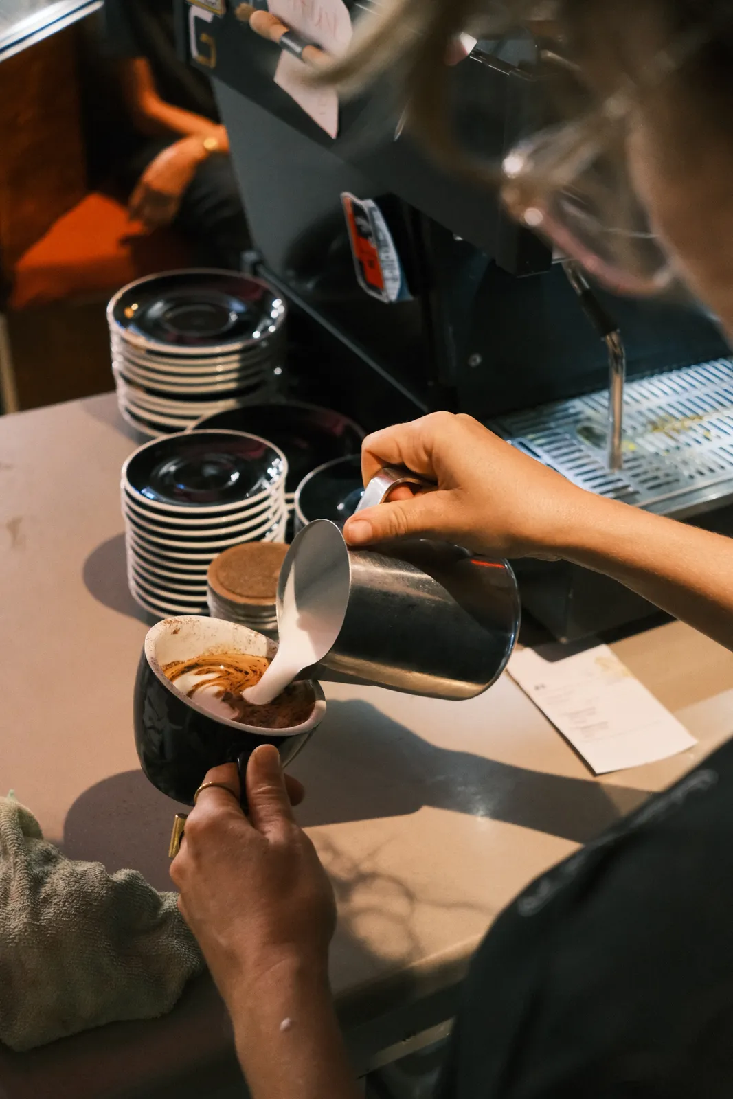 A barista pouring milk into a coffee at the machine.