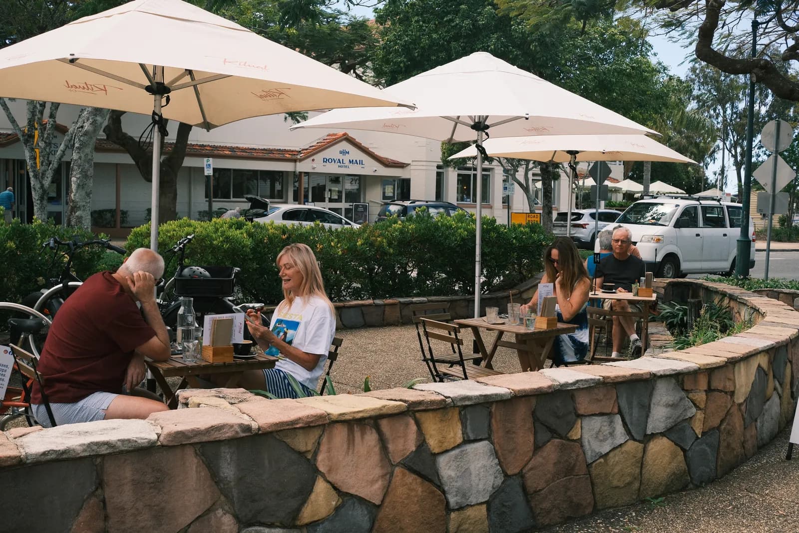 People at tables under white umbrellas on the terrace.